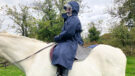 Rider wears Reincoat Lite on horse with hood up, viewed from the side