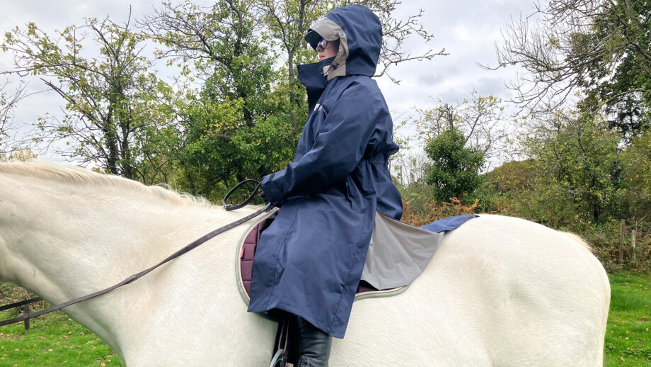 Rider wears Reincoat Lite on horse with hood up, viewed from the side