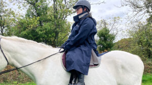 Rider wears Reincoat Lite on horse, viewed from the side