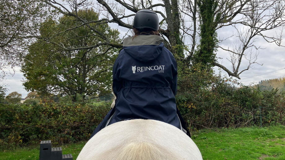 Rider wears Reincoat Lite on horse, viewed from the back