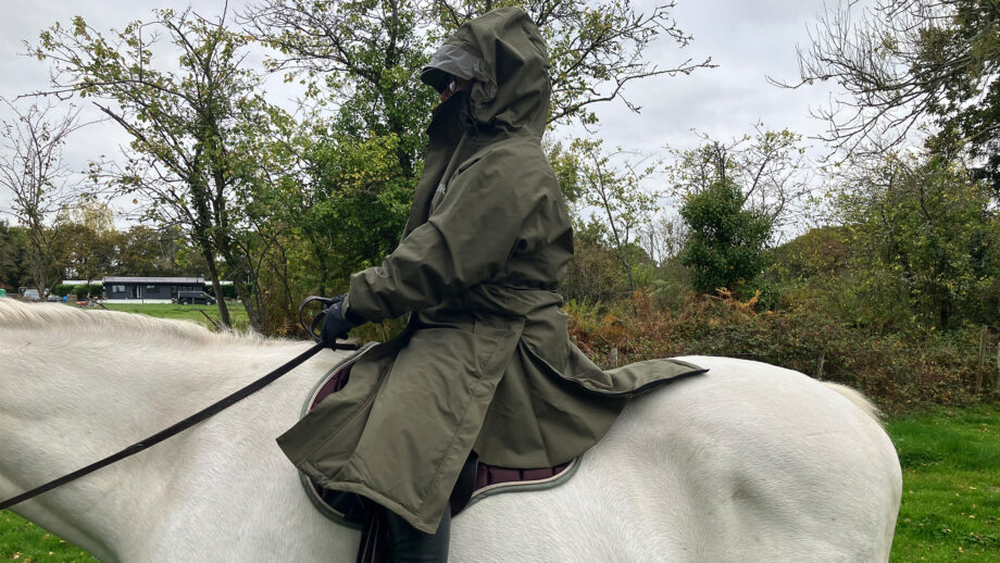Rider wears Reincoat Pro Robe on a horse with the hood up, viewed from the side