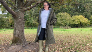 Lady wears Reincoat Pro by a tree un zipped