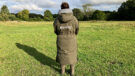 Lady wears Reincoat Pro in a field, viewed from the back