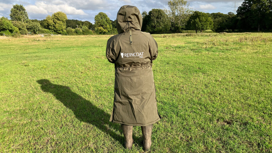 Lady wears Reincoat Pro in a field with hood up, viewed from the back