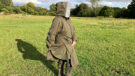 Lady wears Reincoat Pro in a field, showing reinshield feature viewed from the side