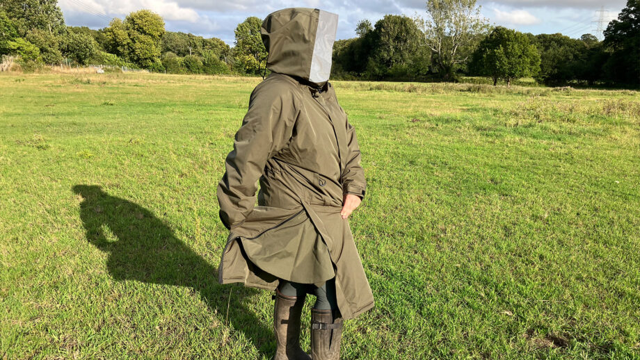 Lady wears Reincoat Pro in a field, showing reinshield feature viewed from the side