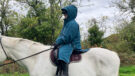 Rider wears Two Bare Feet Hi-Vis Lightweight Riding Robe on a horse with the hood up, viewed from the side