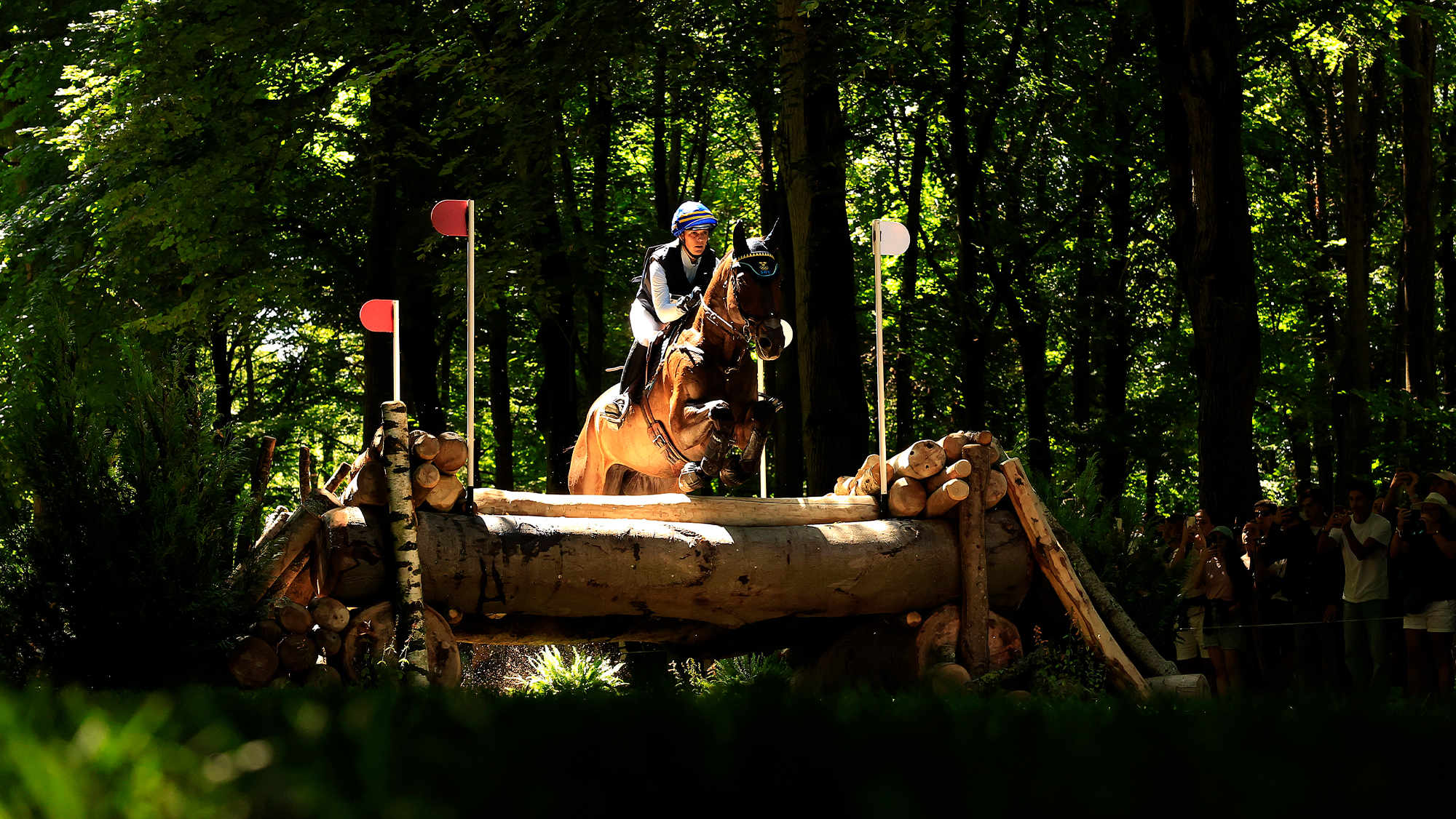 Frida Andersen riding cross-country at the Paris Olympics, showing a fence ridden through changing light