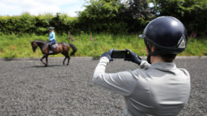 Person on the ground filming rider on horse in background for AI horse training