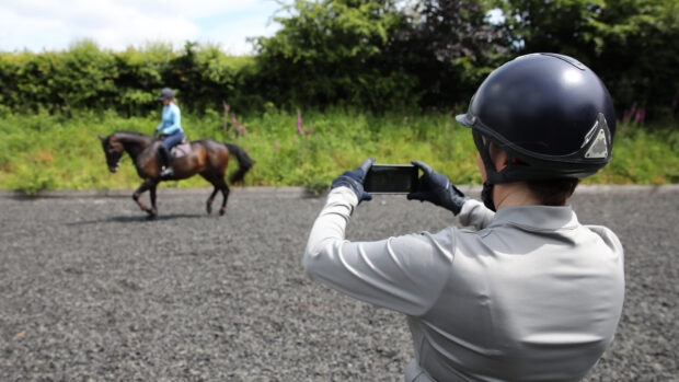 Person on the ground filming rider on horse in background for AI horse training