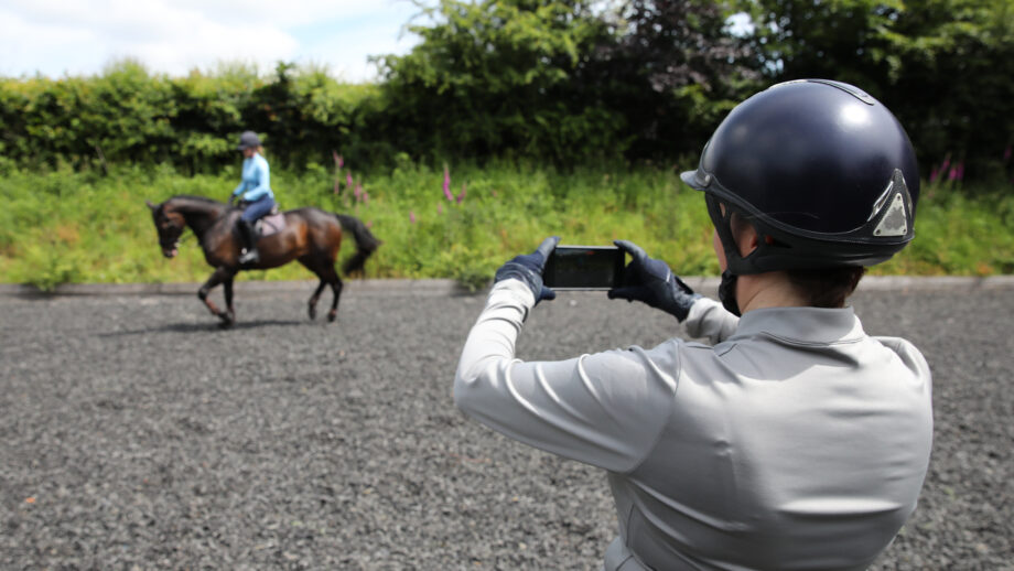 Person on the ground filming rider on horse in background for AI horse training