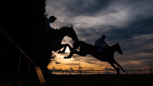 Image shows a silhouette of two racehorses jumping over a fence at a point-to-point.