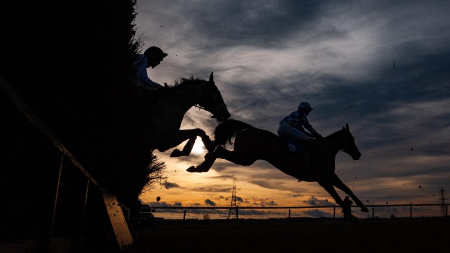 Image shows a silhouette of two racehorses jumping over a fence at a point-to-point.