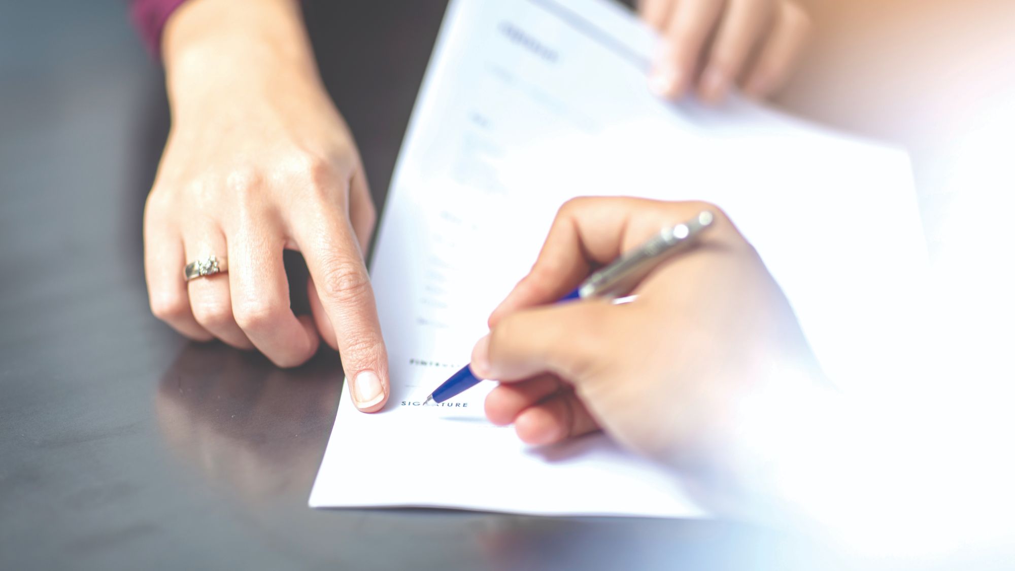 A document with one hand pointing and another signing with a pen