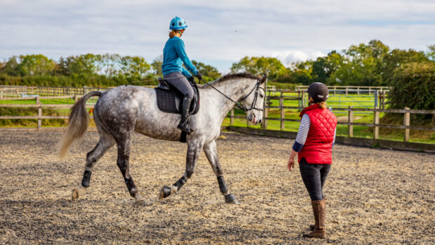 Horse rider wearing horse riding clothes and learning to ride with teacher in the foreground