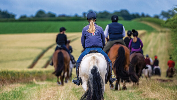 A group of horse riders out on a summer evening for hack by a ripening cornfield against a dark sky.
