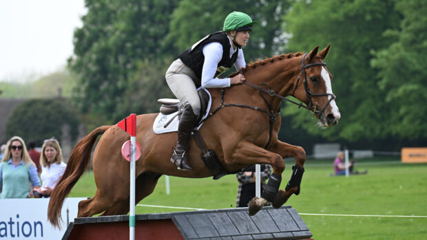 Rider wearing a body protector and jumping cross-country fence at Badminton Grassroots