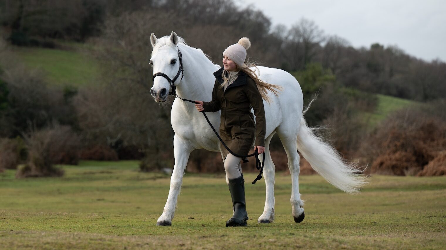 Harlow leads her grey pony Panda across a field in the New Forest