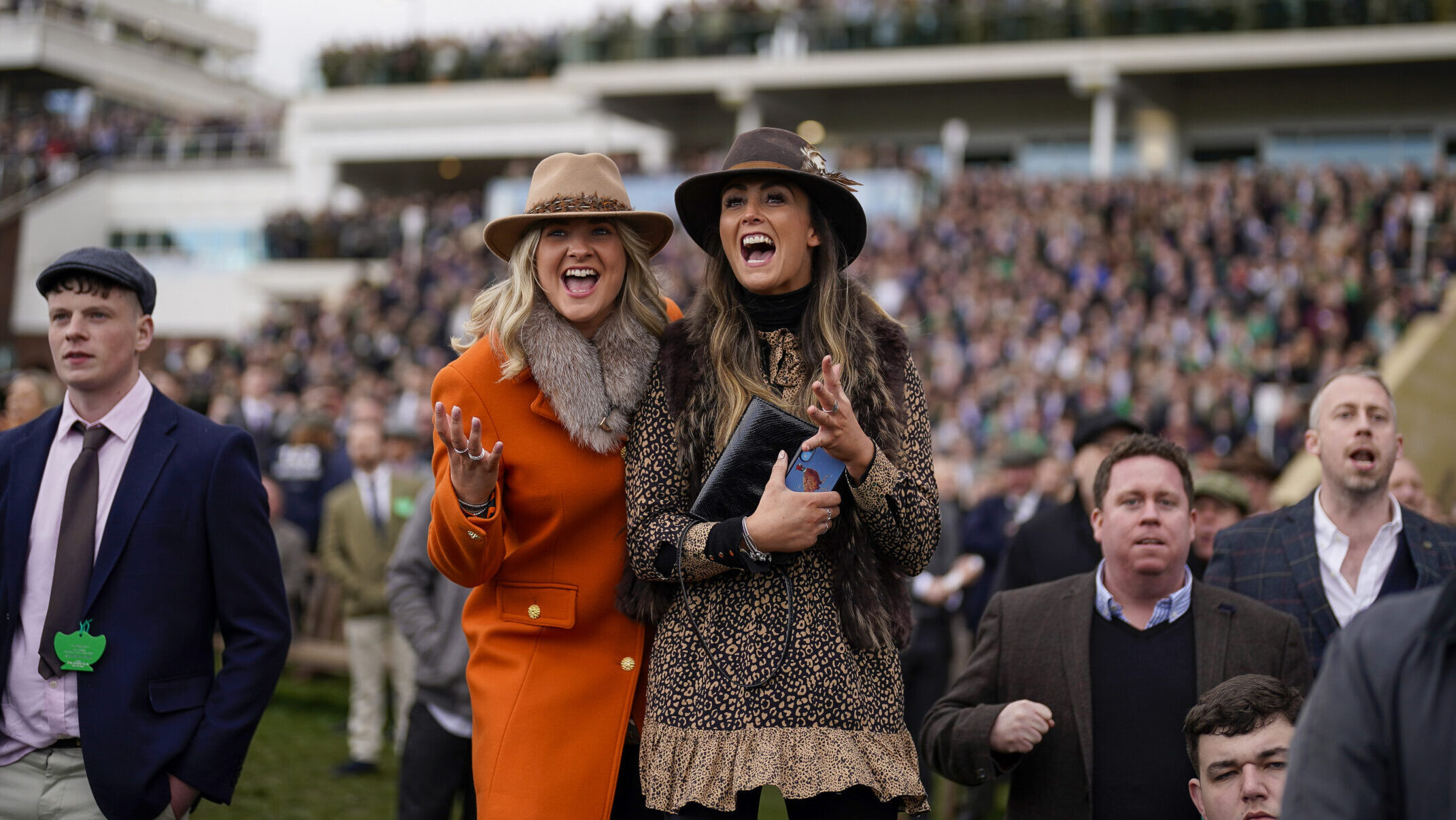 Two ladies in front of the crowd at Cheltenham races, cheering on the winner