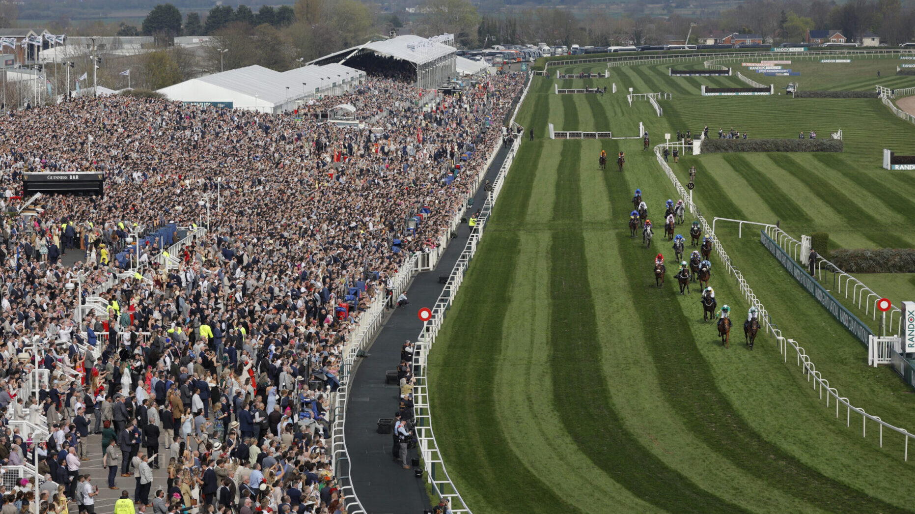 The huge Aintree crowd watches the home straight and a view of the finishing post at The Grand National meeting