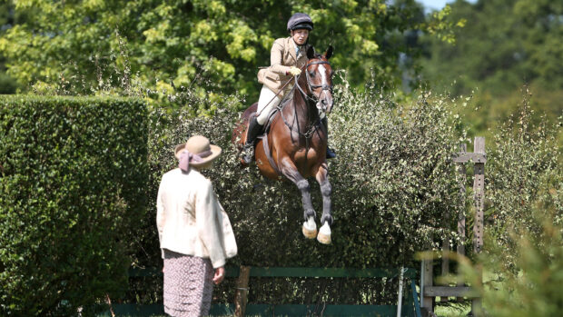 Rider demonstrating how to jump a bullfinch towards camera with working hunter judge in foreground