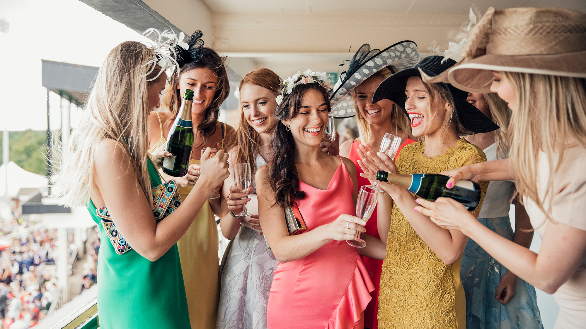 A group of young women opening a bottle of champagne on ladies day. Smiling and laughing with friends.