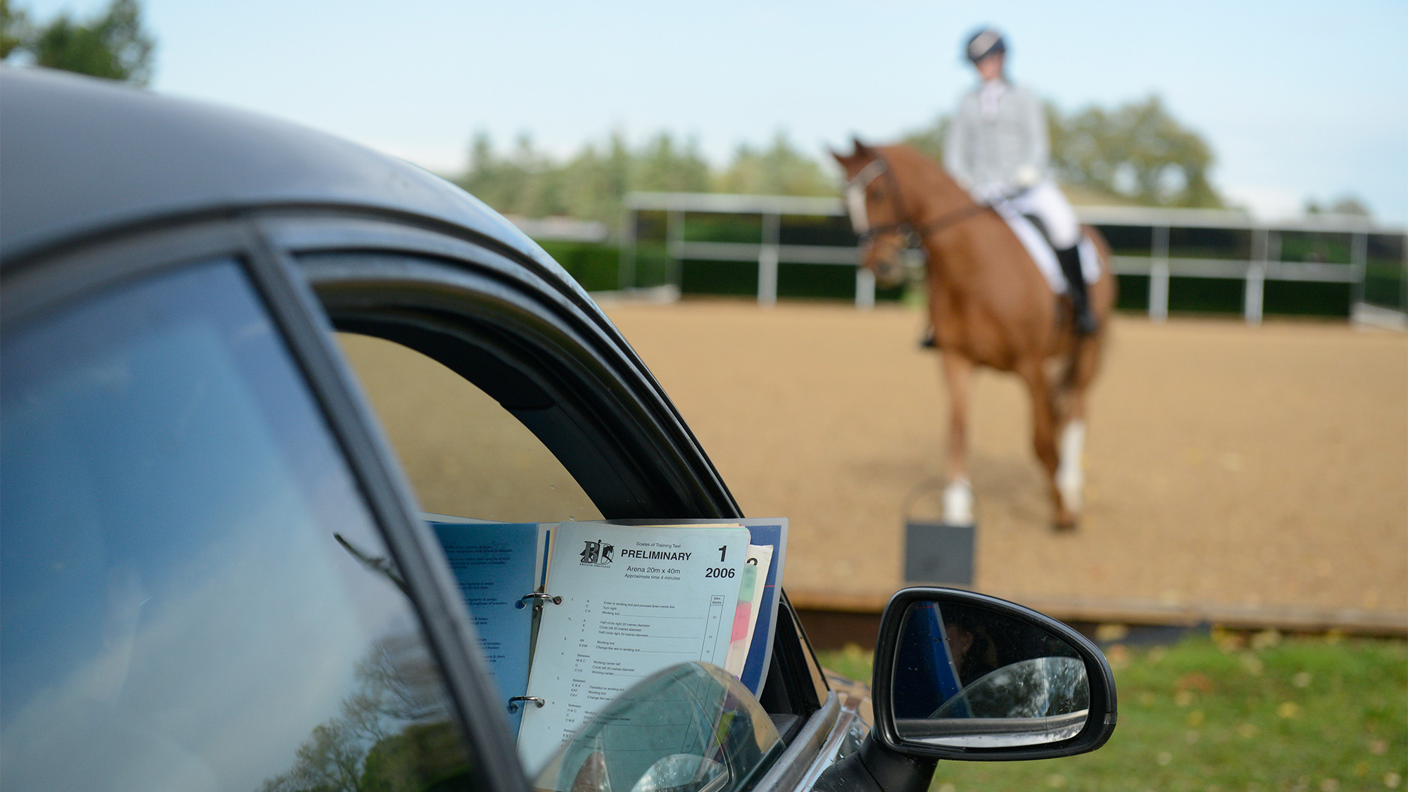 Dressage judge’s car with rider and horse riding test in the background