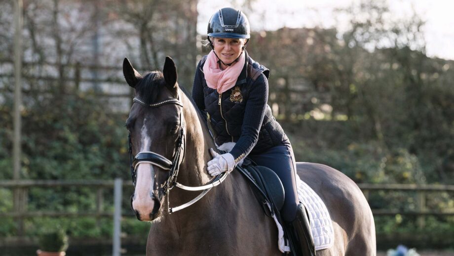Dressage rider Louise Bell pats her rising star dressage horse Peaky Blinder on the neck as they both look at the camera during a magazine shoot at home