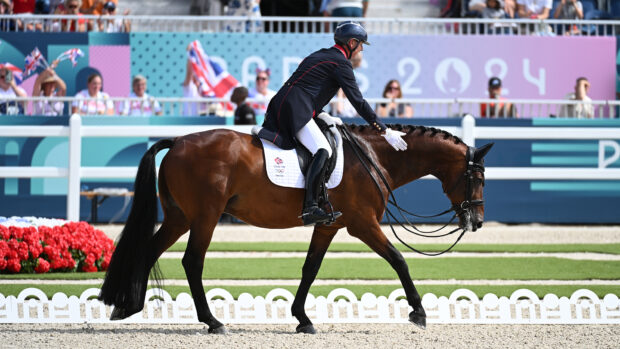 Carl Hester pats Fame's neck with a white gloved hand as they leave the arena on a loose rein after their freestyle at the Paris 2024 Olympic Games.