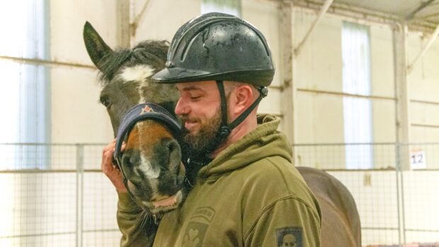 Image shows a man cuddling a horse