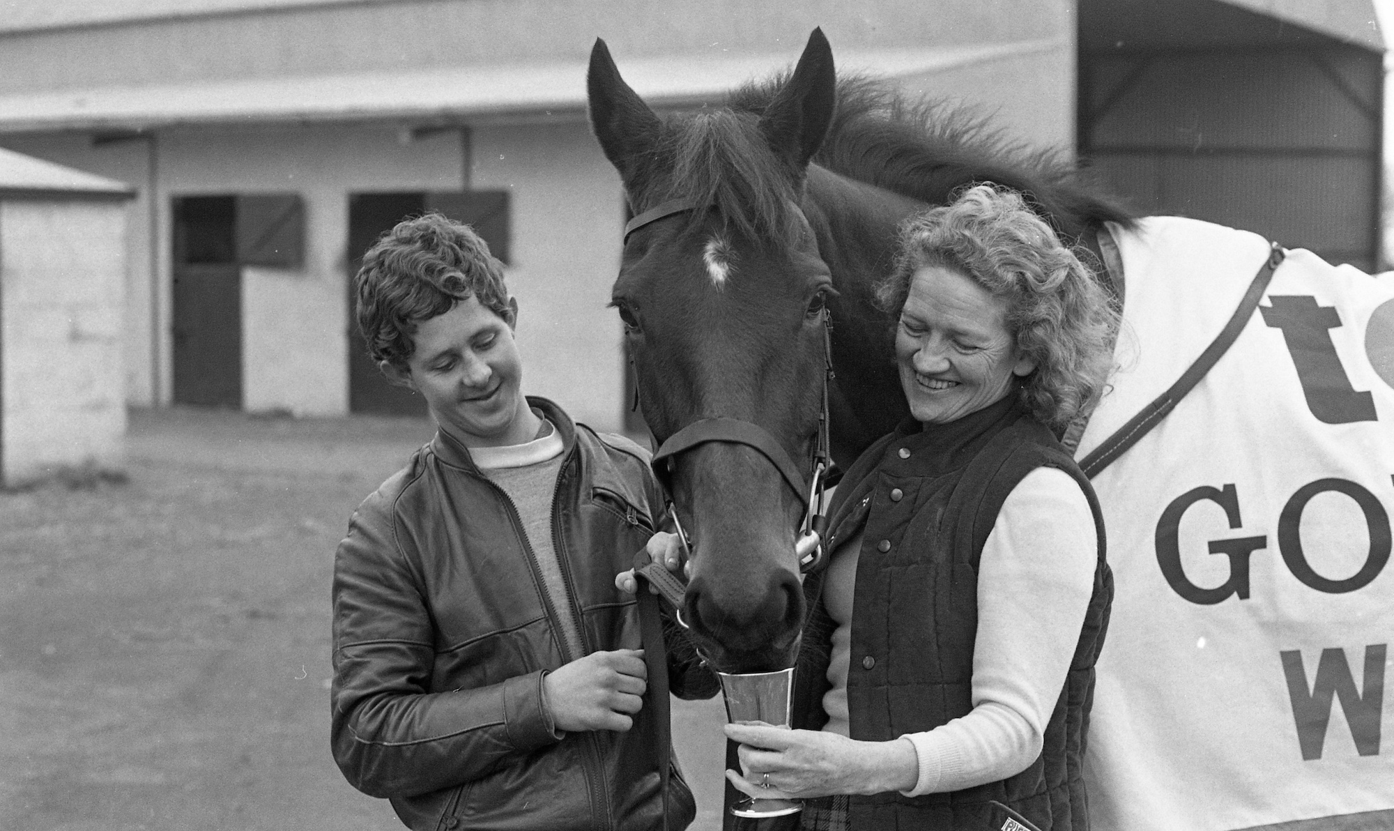 Dawn Run with her groom and Maureen Mullins the trainer's wife. The horse is drinking out of a goblet. 