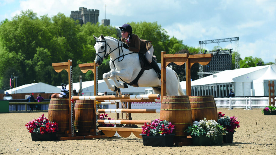 Grey working hunter pony Ellas Melody jumps a fence at Windsor Horse Show with the castle visible in the background