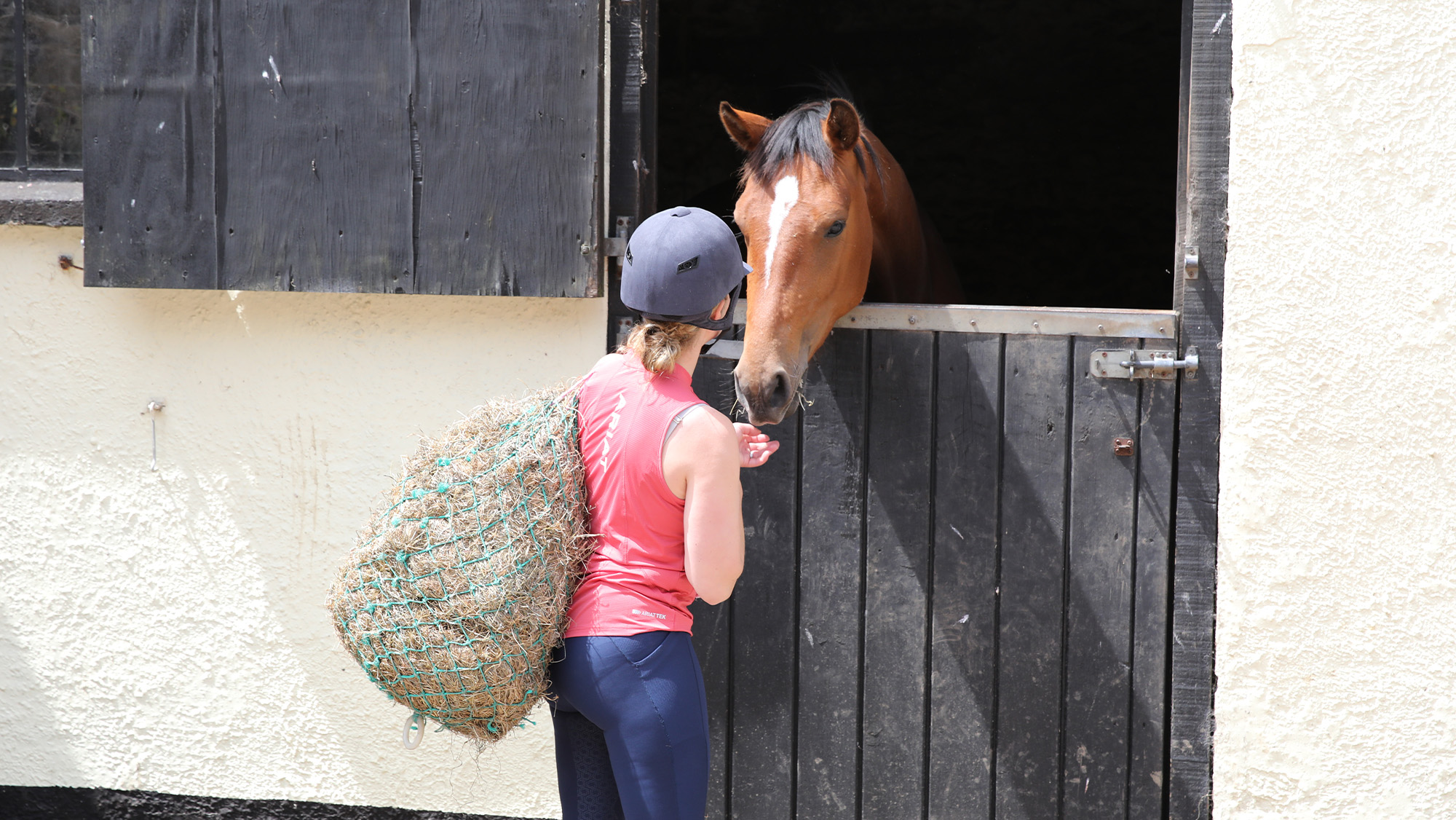 Female carrying haynet to horse in stable