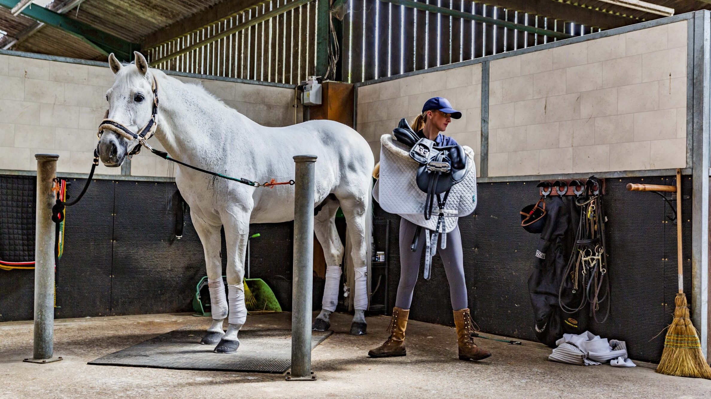 Groom tacking up horse in cross ties on livery yard