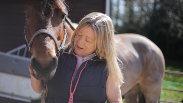 A lady looking at her pony who is stood alongside wearing a headcollar.