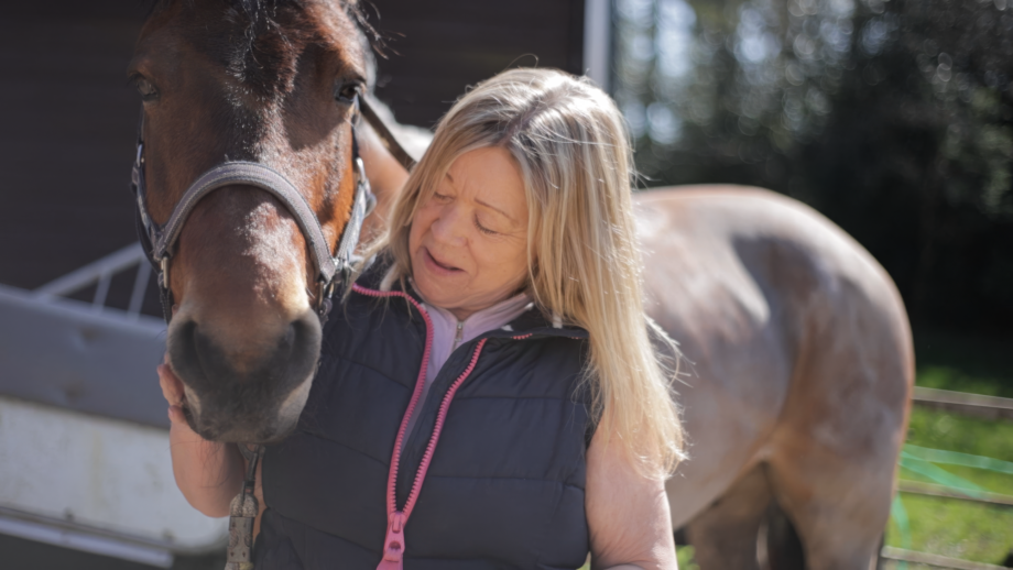 A lady looking at her pony who is stood alongside wearing a headcollar.
