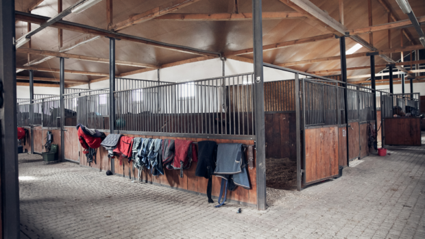Stables inside a barn with horse rugs hanging up