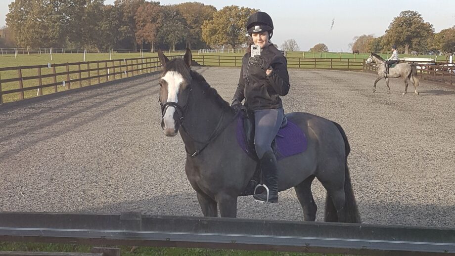 Woman one a dark bay horse taking a photo in an arena mirror