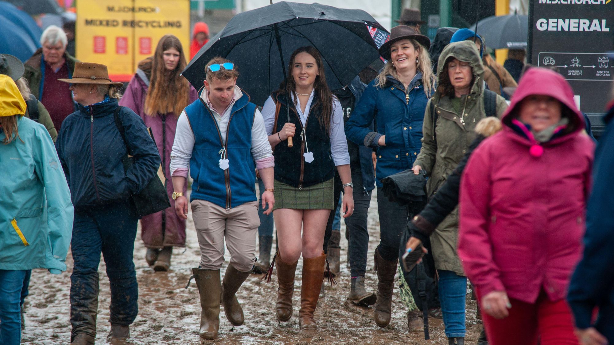 A rainy day at Badminton Horse Trials. Spectators walk towards the camera through mud.