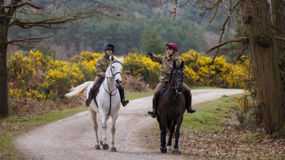 Two British Army soldiers navigate through the woods on horses