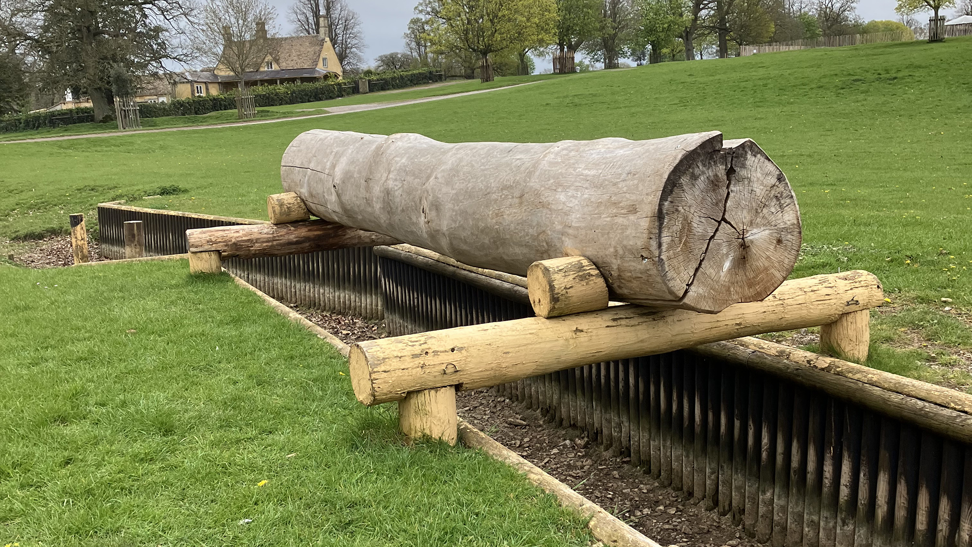 A raised log suspended over a large ditch with wooden reinforced walls