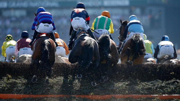 General view of horses and riders clearing a fence in the Grand National