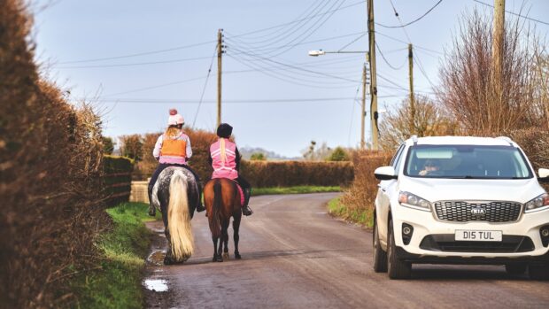 Riders and horses in high-vis on a road with a car passing