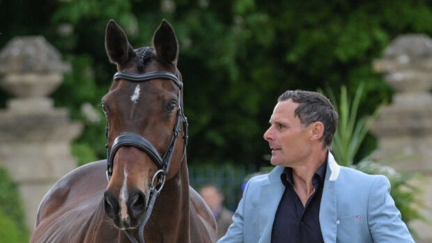 Alex Bragg looks towards his Badminton ride Quindiva, who is a bay mare with pricked ears wearing a snaffle bridle, as he presents her for the first horse inspection at Badminton