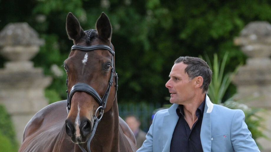 Alex Bragg looks towards his Badminton ride Quindiva, who is a bay mare with pricked ears wearing a snaffle bridle, as he presents her for the first horse inspection at Badminton