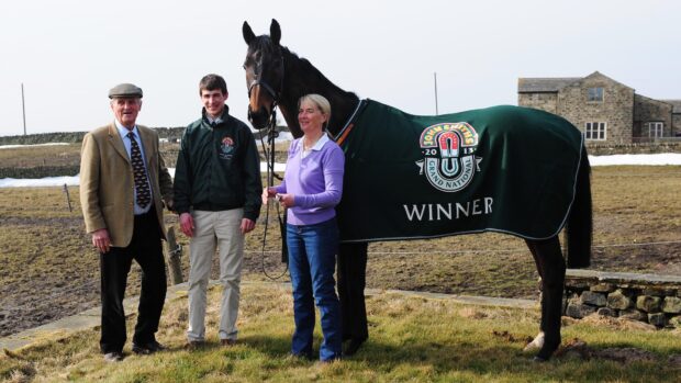 Auroras Encore at home after his National win, wearing his winner's rug with his trainers and jockey