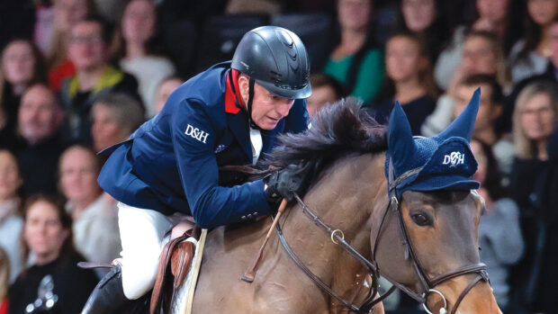 John Whitaker crouches over his horse's neck as they jump a large fence at London International