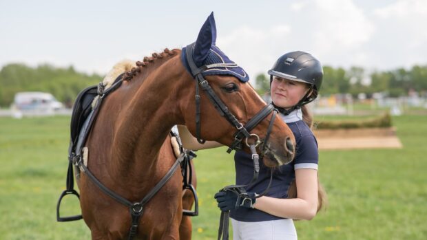 Young girl in competition kit standing with horse
