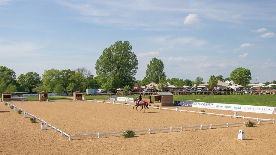 A distant shot of a dressage arena at Hickstead wth a horse cantering across the diagonal in front of the judges' huts.