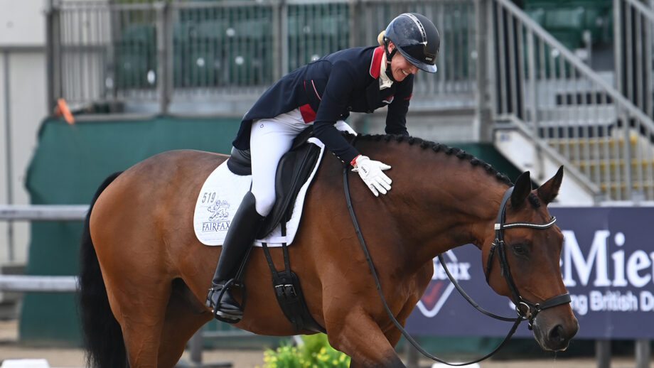 British dressage rider Laura Tomlinson leans forward in the saddle to rub her bay horse on the neck after their dressage test.